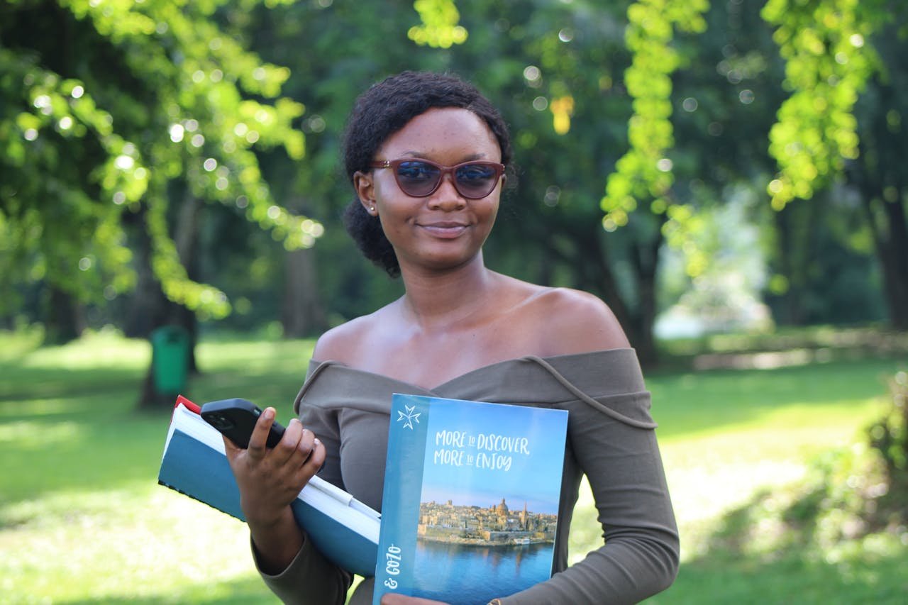 African student enjoying a sunny day at a park in Kumasi, Ghana, while holding study books.