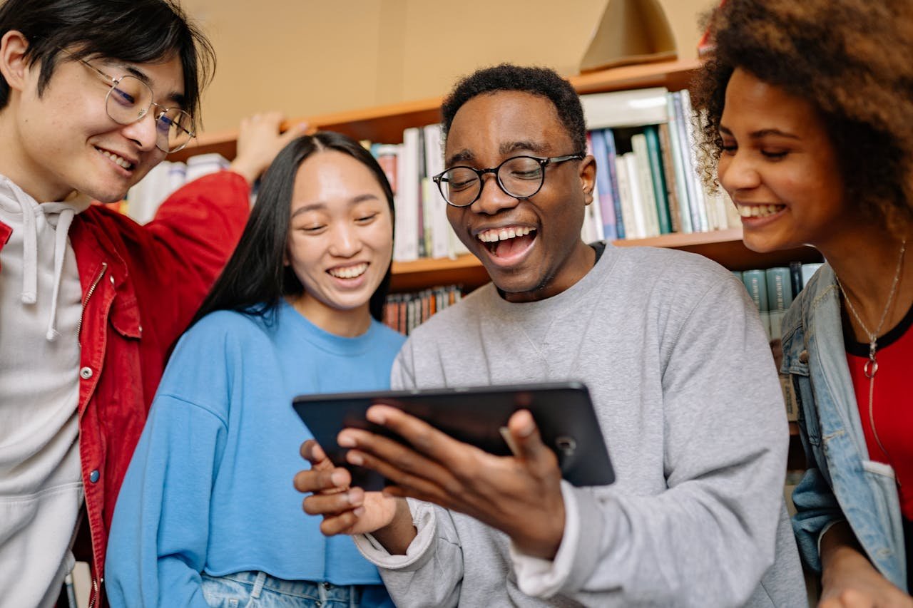 A group of diverse students enjoying studying together in a library, using a digital tablet.